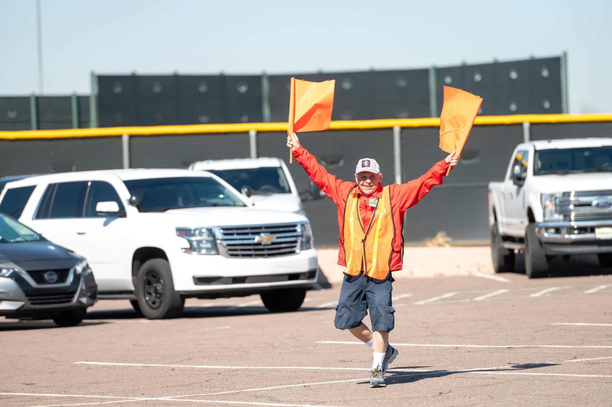 Tempe Diablos volunteer waving flags to direct cars in the Tempe Diablo Stadium parking lot